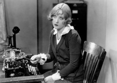 Marion Davies sitting in front of a typewriter.  