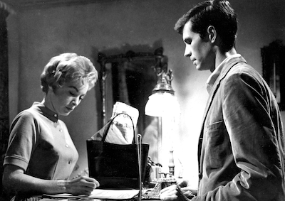 A woman signing in at a motel desk staffed by a man.