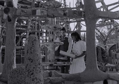 A young man and woman smiling at the Watts Towers.