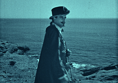 A man in period costume standing by the ocean. 