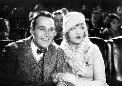 Actors William Haines and Marion Davies sitting in a theater.