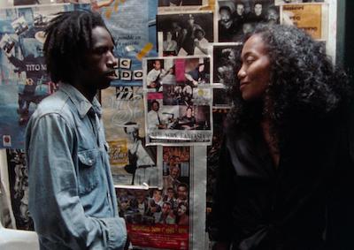 Two people talking in a room plastered with posters.