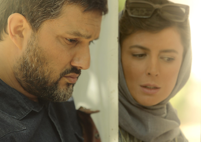 A man and a woman standing on the opposite sides of a door, both looking down.