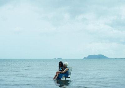 A woman and a girl sitting in a chair in the ocean.