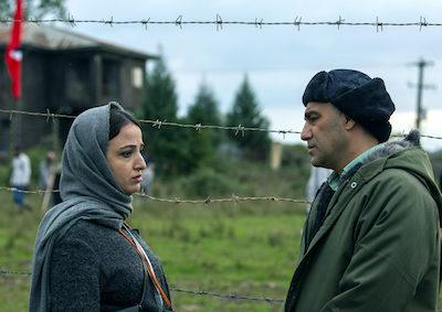 A woman and a man speaking by a barbed wire fence.