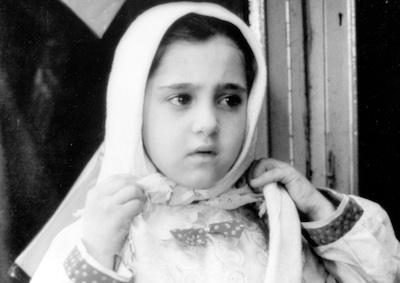 A little girl tying a head scarf.