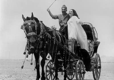 Two people standing in a horse carriage.