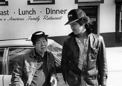 Two men leading against a car outside a Chinese American restaurant.