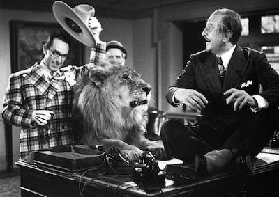 Harold Lloyd tipping a hat with a lion by his side, startling a man.