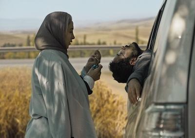 Two people by a car in a rural landscape.