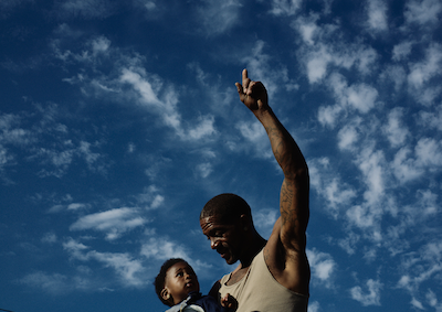 A man pointing to the sky and holding a baby.