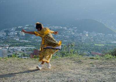 A person dancing on a hill that overlooks a city.
