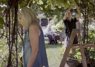 A person standing, a person trimming a vine, and a person sitting in a garden.