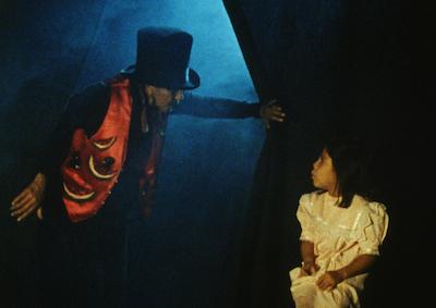 A man wearing a top hat and a vest decorated with watermelons talking to little girl.