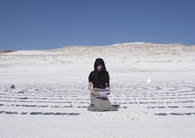 A woman surround by sheets of paper in a desert landscape.