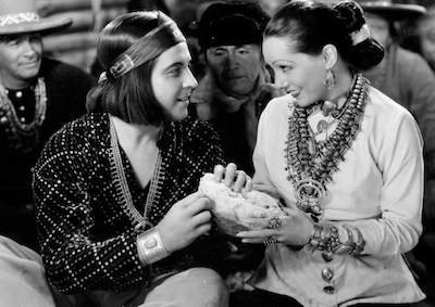 Actors Ramon Novarro and Lupe Velez smiling and sharing bread.