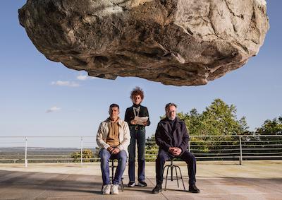 Three people beneath a large, dangling rock.