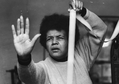 Sarah Maldoror holding a strip of film and raising a palm.