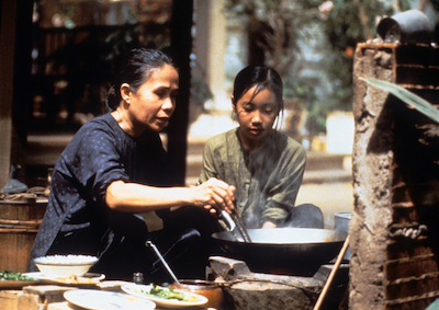 A young girl watching an older woman cook.
