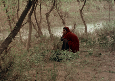 A woman crouching by a stream.