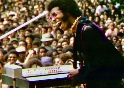 A man playing keyboard and singing to a large crowd.