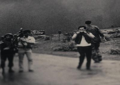 A man holding a camera in a war zone.