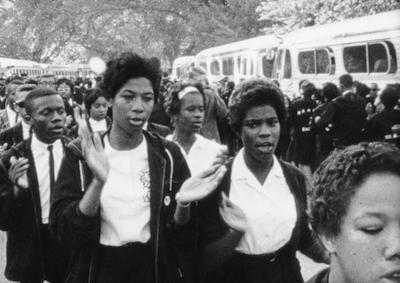 A large crowd clapping and chanting alongside a row of buses.