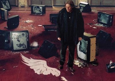 Actor Willem Dafoe standing among broken TVs.