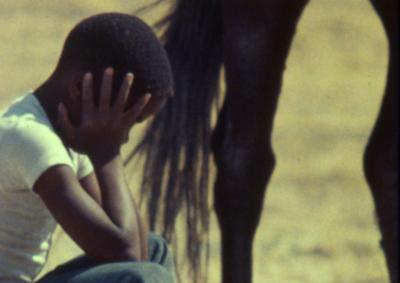 A boy sitting with his hands on his head next to a horse.