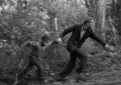 A boy and man holding hands and running among trees.