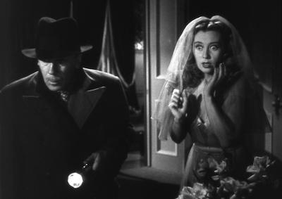 A frightened Joan Blondell wearing a wedding veil next to a man holding a flashlight.