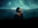 A person looking up at dark, cloud-filled sky. 