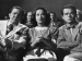 Merle Oberon sitting among a crowd.