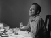 James Baldwin sitting at a table and smiling.