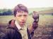 A boy in a field holding a bird in his hand.