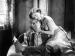 Actor Lon Chaney holding a cigarette between his toes while actor Joan Crawford embraces him.