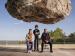 Three people beneath a large, dangling rock.