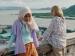 Two women leaning against a wall, with the sea in the background.